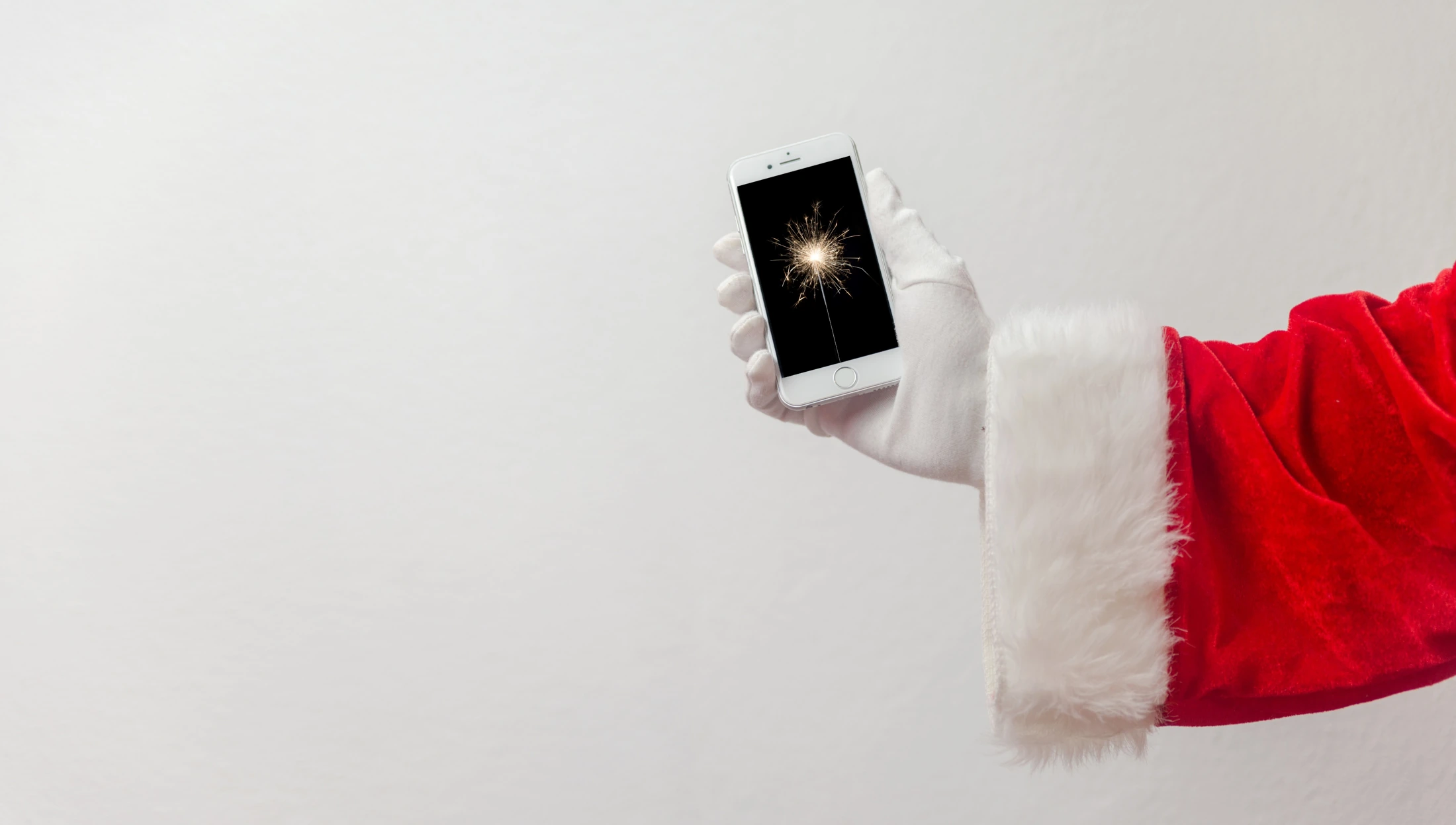 A sparkler on a phone, held by a hand in a Santa sleeve